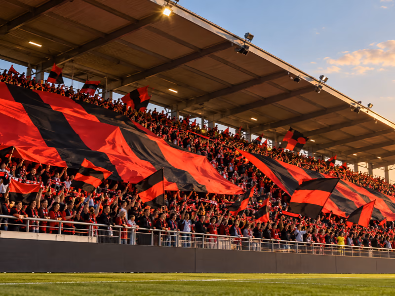 Tribune de supporters agitant de grands drapeaux rouge et noir au coucher du soleil